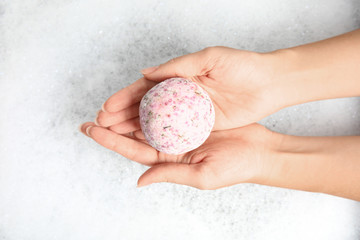 Woman holding color bath bomb over foam, top view