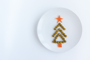 Fir tree made of peas and carrots on white plate on rustic white table background. New year and christmas concept, creative idea of celebratory meal
