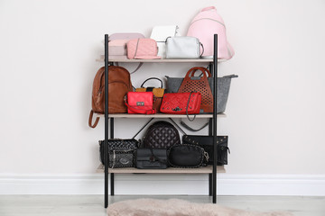Shelving unit with stylish purses near white wall. Element of dressing room interior