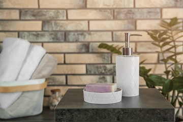 Dish with soap bars and bottle of shampoo on table near brick wall. Space for text