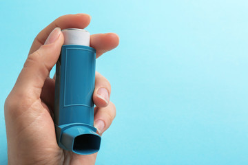 Woman holding asthma inhaler on color background. Space for text