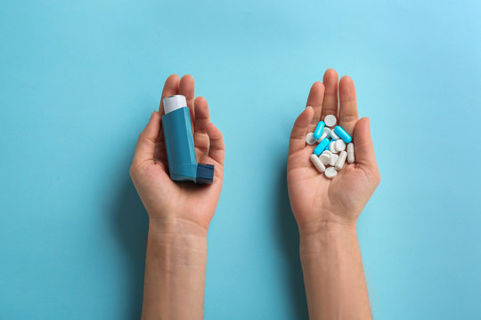 Woman holding asthma inhaler and pills on color background, top view