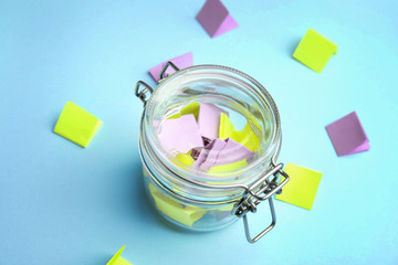 Glass jar and paper pieces for lottery on color background