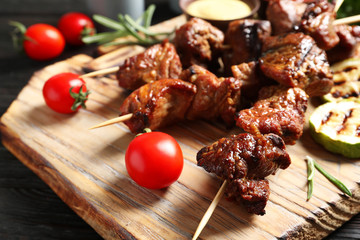 Delicious barbecued meat served with garnish and sauce on wooden board, closeup