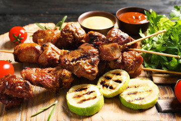 Delicious barbecued meat served with garnish and sauces on wooden board, closeup
