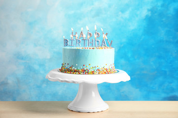 Fresh delicious birthday cake with candles on stand against color background