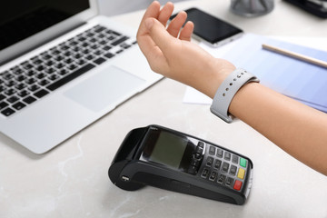 Woman using terminal for contactless payment with smart watch at table