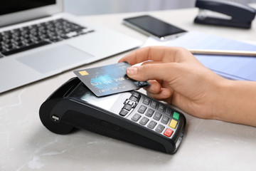 Woman using terminal for contactless payment with credit card at table