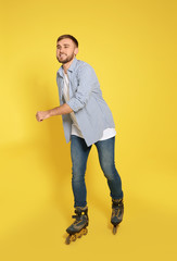 Young man with inline roller skates on color background