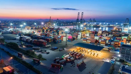 Container-LKW fahren zum Terminal-Container-Lager am Seehafen mit Kranbrücke, die Container in der Abenddämmerung zum Logistik-Import-Export oder -Transport auf das Containerschiff lädt. © Pawinee