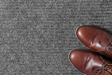 Brown classic shoes on gray doormat, top view. Space for text