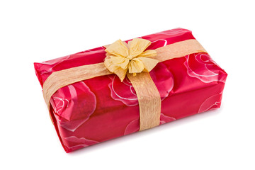 Gift box wrapped in red rose cellophane, decorated with ecru raffia ribbon and bow isolated on the white background