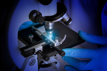 Researcher hands in blue rubber gloves using the microscope in laboratory to study a sample for developing a new drug and new substance.