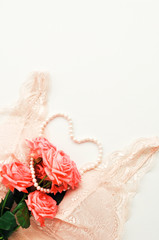 Delicate feminine theme. Pink coral roses trend color on a pale pink bra and pearl necklace on a white background. top view. close up. Stylish lingerie flat lay.selective focus