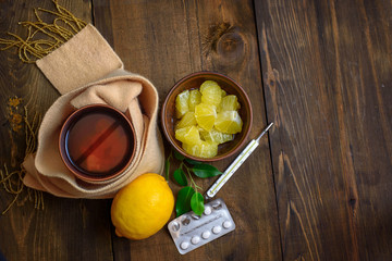Concept illness, colds, cure, fall and winter. Tea with lemon, thermometer, pills and a knitted scarf. Top View.