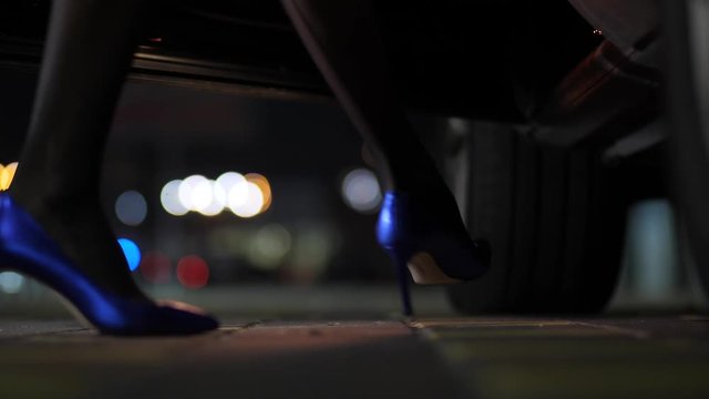 Close-up beautiful slim female legs in blue high heel shoes getting into car at night over citylights bokeh background 4K Slow Mo