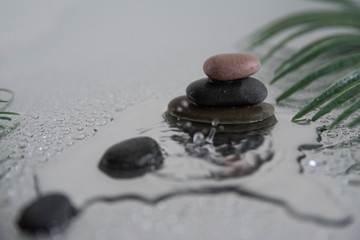 Pyramids of gray zen pebble meditation stones with green leaves on the mirror water reflection background with water splash. Concept of harmony, balance and meditation, spa, massage, relax