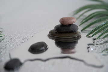 Pyramids of gray zen pebble meditation stones with green leaves on the mirror water reflection background. Concept of harmony, balance and meditation, spa, massage, relax