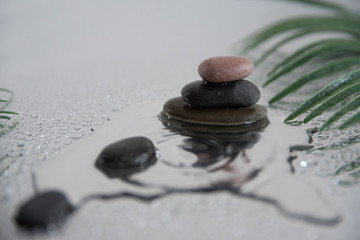 Pyramids of gray zen pebble meditation stones with green leaves on the mirror water reflection background with water splash. Concept of harmony, balance and meditation, spa, massage, relax