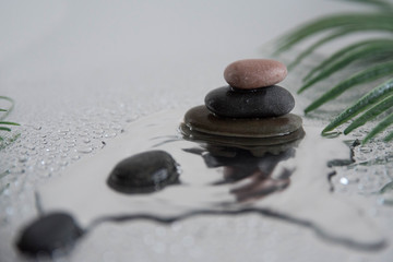 Pyramids of gray zen pebble meditation stones with green leaves on the mirror water reflection background. Concept of harmony, balance and meditation, spa, massage, relax