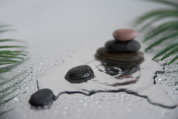Pyramids of gray zen pebble meditation stones with green leaves on the mirror water reflection background with water splash. Concept of harmony, balance and meditation, spa, massage, relax