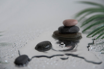 Fototapeta na wymiar Pyramids of gray zen pebble meditation stones with green leaves on the mirror water reflection background with water splash. Concept of harmony, balance and meditation, spa, massage, relax