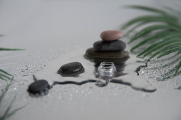 Pyramids of gray zen pebble meditation stones with green leaves on the mirror water reflection background with water splash. Concept of harmony, balance and meditation, spa, massage, relax