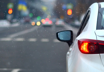 White car stopped on a traffic light in a city. Winter snowy weather.