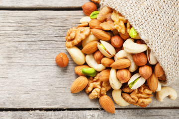Mix of different nuts in a wooden cup against the background of fabric from burlap. Nuts as structure and background, macro. Top view.
