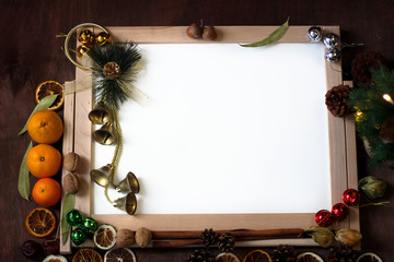 Top view of Christmas decor with copy space area. Christmas objects: dried sliced orange, mandarines, cinnamon, pine cone, fir branch, cup coffee, cheesecake, walnut, golden Christmas bells
