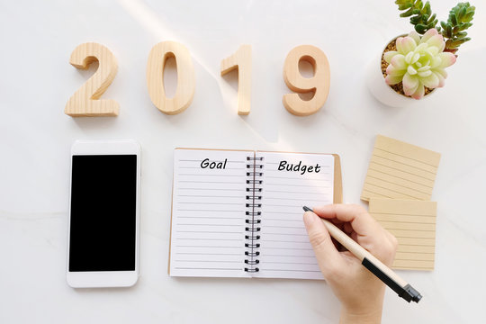 2019 budget word on notebook paper background and smart phone on white marble background, financial concept, business strategy