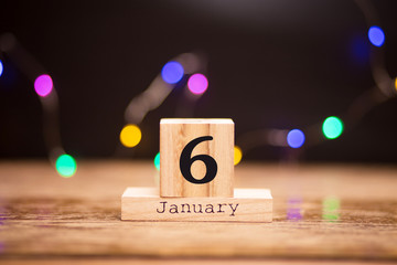 January 6th. Day 6 of January set on wooden calendar on dark background with garland bokeh. Winter time. Holiday Composition