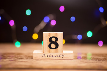 Naklejka premium January 8th. Day 8 of January set on wooden calendar on dark background with garland bokeh. Winter time. Holiday Composition