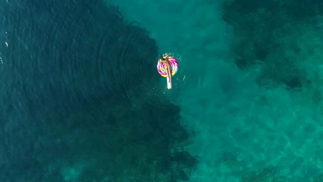 Aerial view of woman floating on inflatable lollipop on Atokos island, Greece.