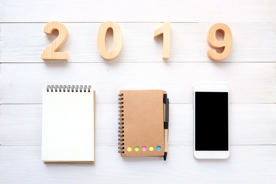 2019 wood letters, blank notebook paper, white smart phone with blank screen and pencil on white wood background, 2019 new year mock up, template with copy space for text, top view