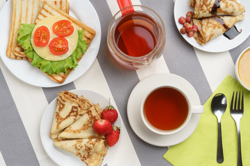 Fresh, tasty breakfast with a sandwich, pancakes and tea on a light background.
