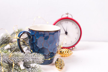 Blue mug with hot tea, coffee or cocoa, fir tree branches  and red clock on white textured  background.