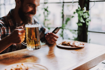 Cheerful bearded man with drink using cellphone at pub