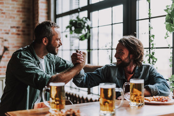 Cheerful friends in arm-wrestling pose looking at each other and smiling