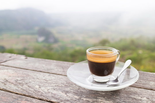 Morning cup of coffee on the wooden table with mountain background at sunrise and sea of mist, image with copy space.