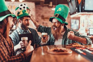 Excited friends celebrating football championship and Saint Patrick Day in pub