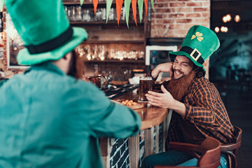 Cheerful man in green leprechaun hat chatting with friend at pub