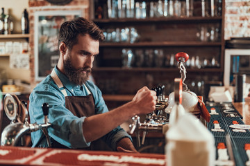 Handsome barman pouring alcoholic drink while standing at the bar counter