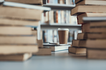 Selective focus of the carton cup of coffee standing near the books
