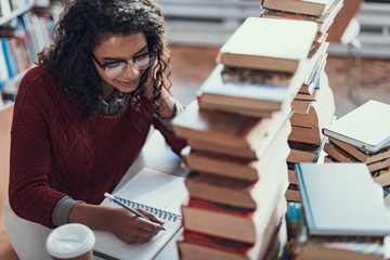 Cheerful student sitting with pile of books and writing