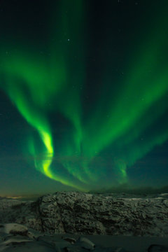 Beautiful stripes of the northern lights, aurora in the night sky above the snow covered hills.