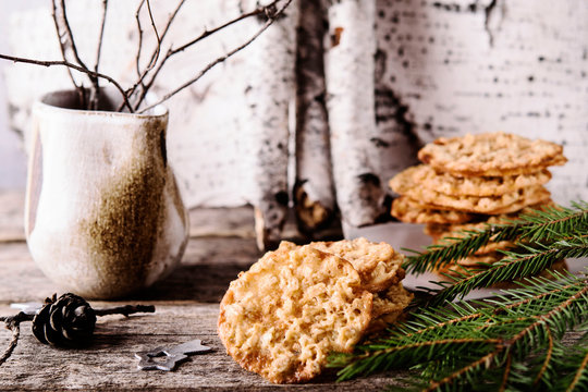 Havreflarn - scandinavian crispy slim oatmeal cookies, fir and birch branches and bark on old wooden background. Fast and easy scandinavian pastry. Cozy winter treat. Hygge. Fika. Christmas
