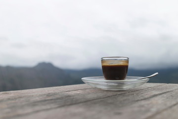 Morning cup of coffee on the wooden table with mountain background at sunrise and sea of mist, image with copy space.