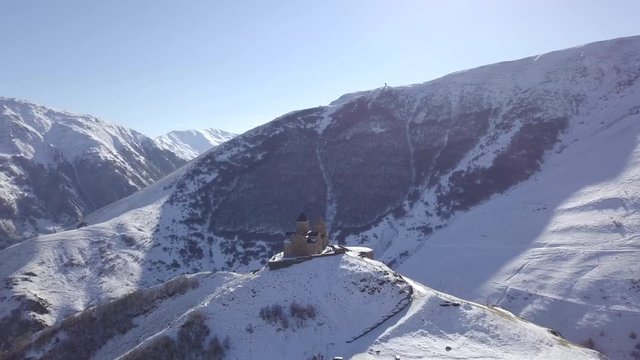 Aerial footage of the Gergeti Trinity Church of the Holy Trinity in the snowy caucasus mountains of Kazbegi, Georgia. Drone flying around lonely medieval church.