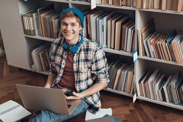 Waist up of positive student sitting on the floor with laptop